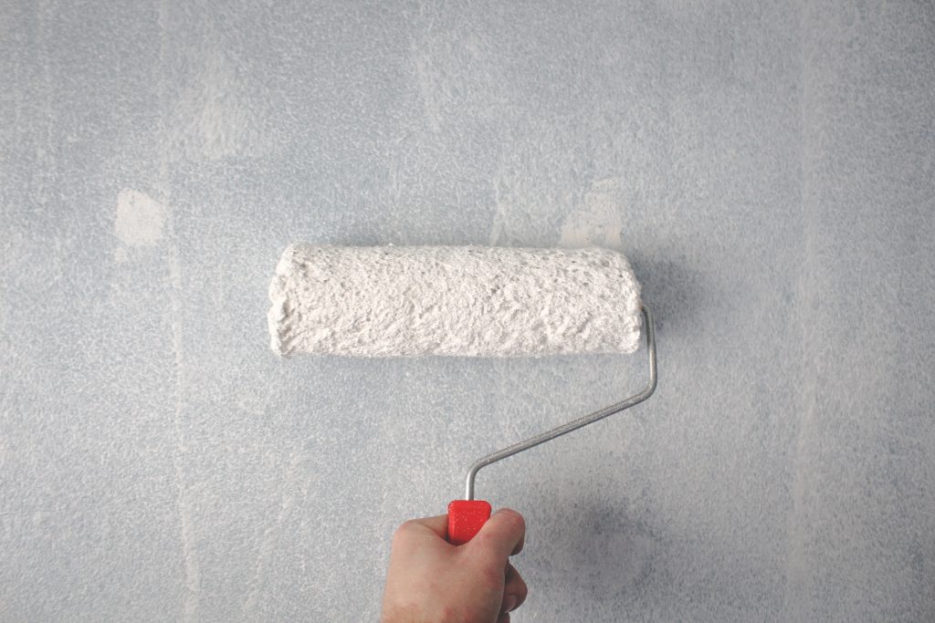 Hand holding white paint roller on a primed wall
